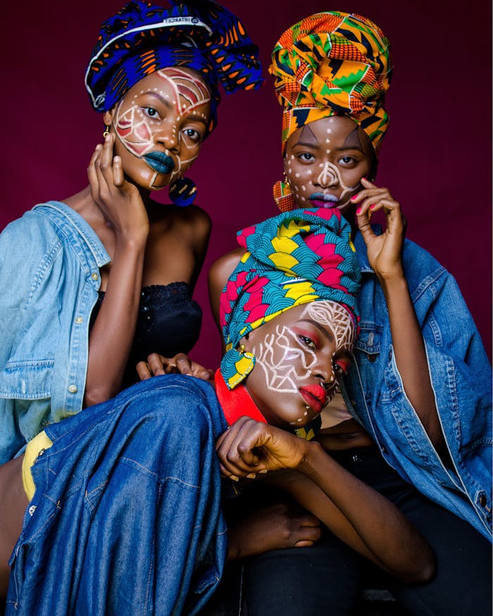About Three women in colorful African outfits with face paint and headdresses celebrating culture.